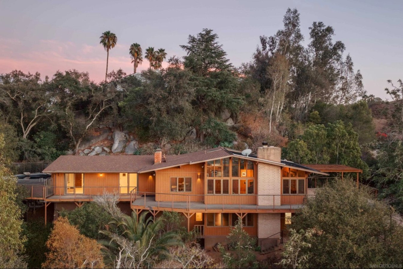 Two-story wood and glass Sim Bruce Richards home at 16208 Orchard Bend Rd, Poway, with a long deck set into a wooded hillside at sunset