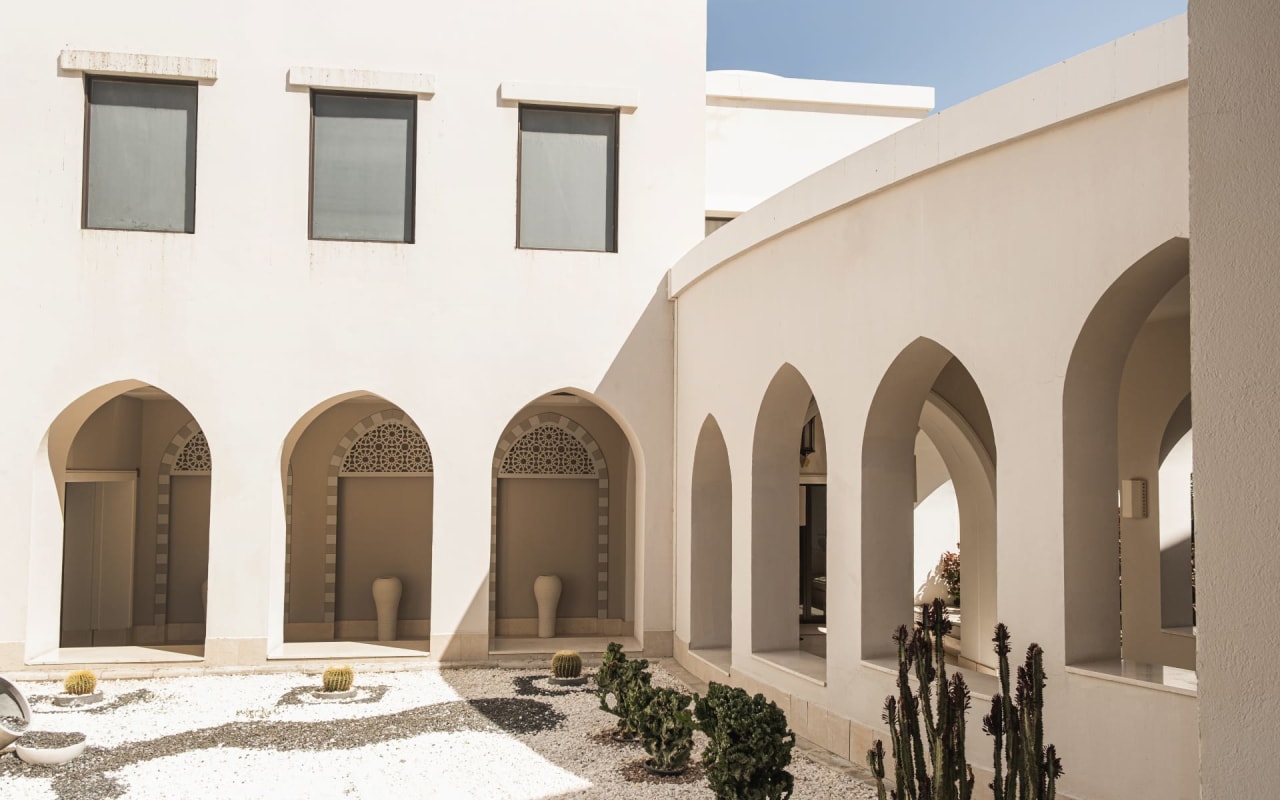 A white building with arches and cactus plants in front of it.