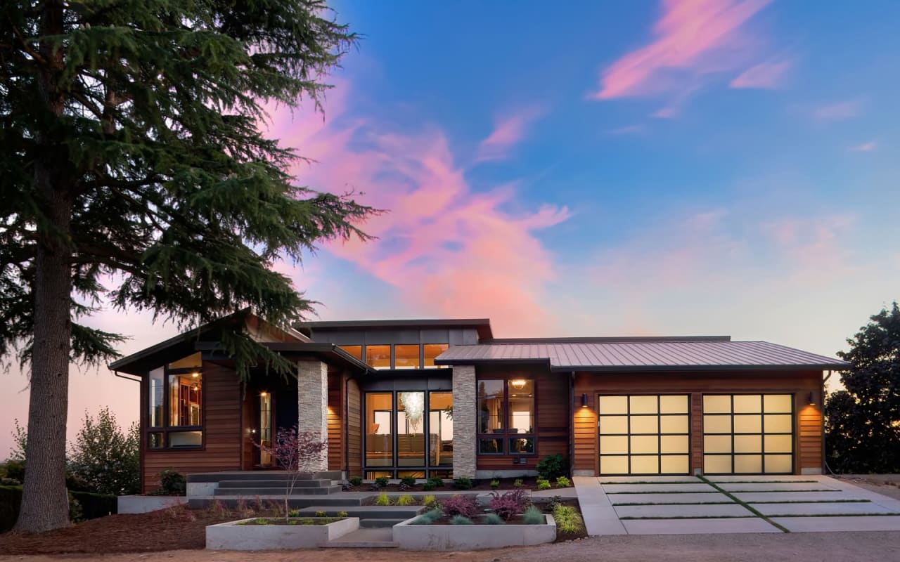 A modern house with a glass garage door and flat roof, bathed in the warm light of a sunset.