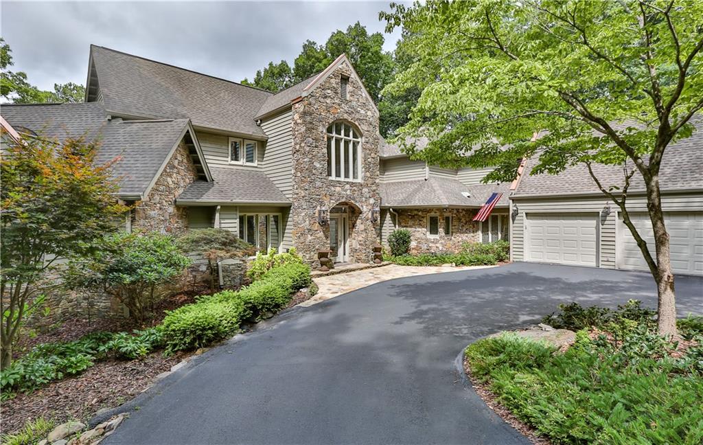 Large stone house with driveway, surrounded by trees.