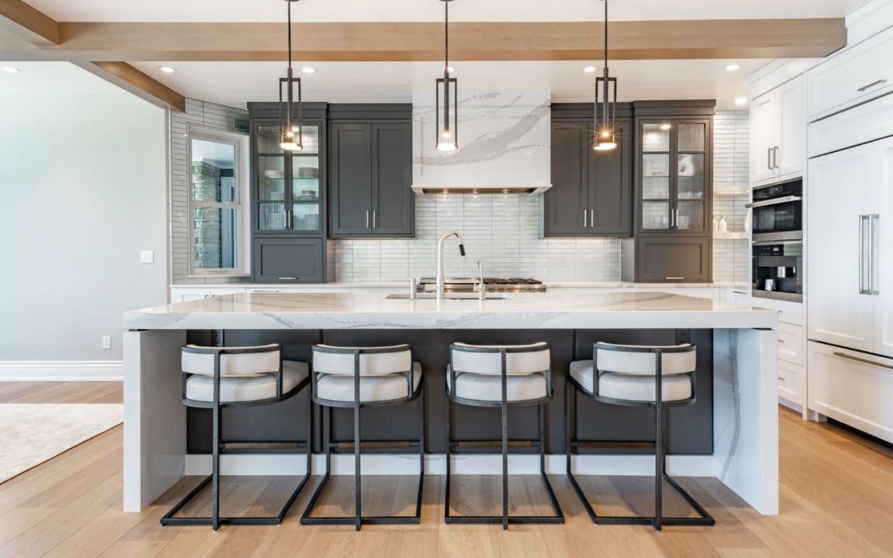 A modern kitchen with a large center island that has a sink, stovetop, and refrigerator.