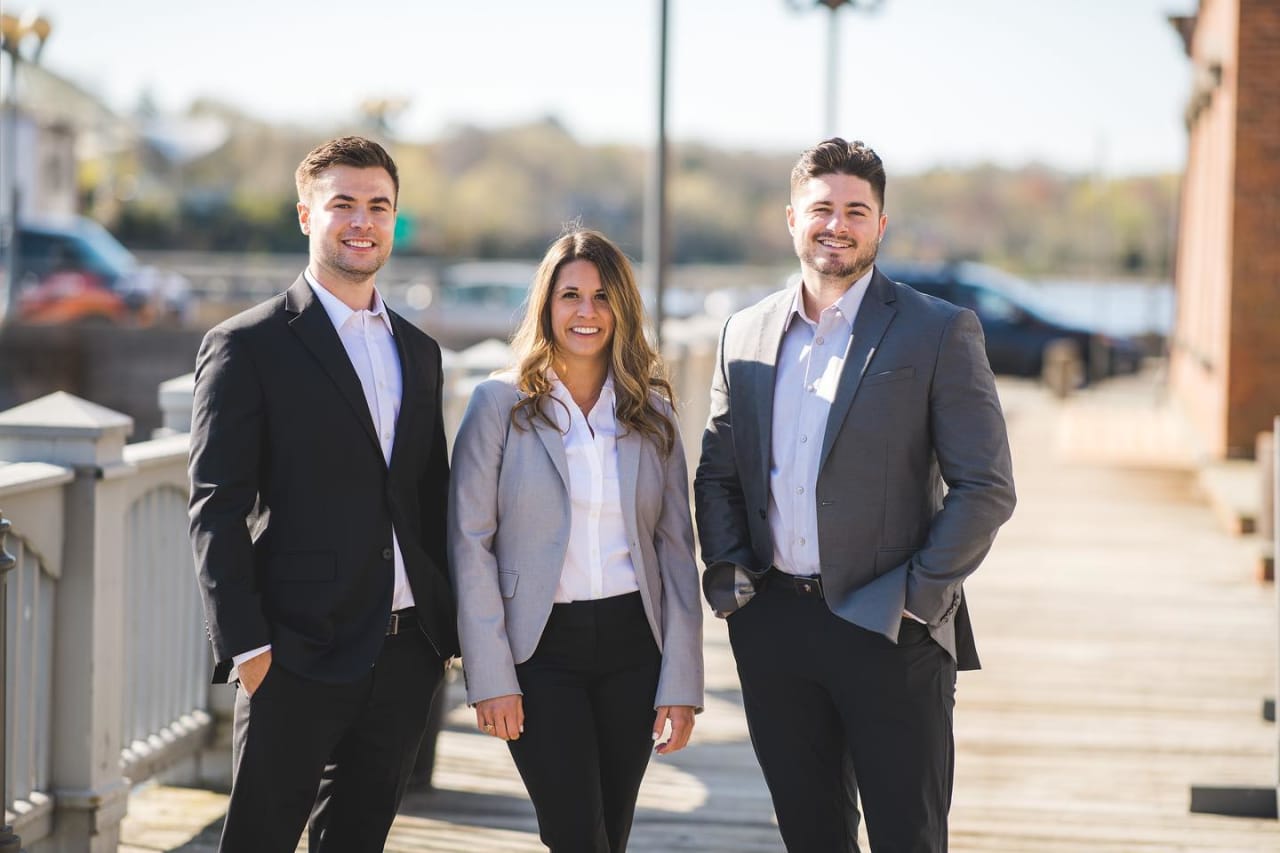 Three real estate team members pose together on a waterfront boardwalk.
