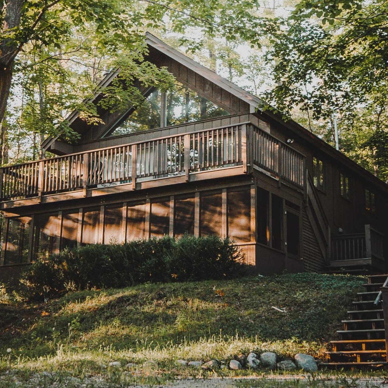 A wooden cabin with a large deck in the woods.