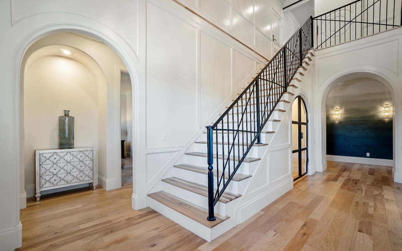 A hallway with a wooden staircase that has a black railing.