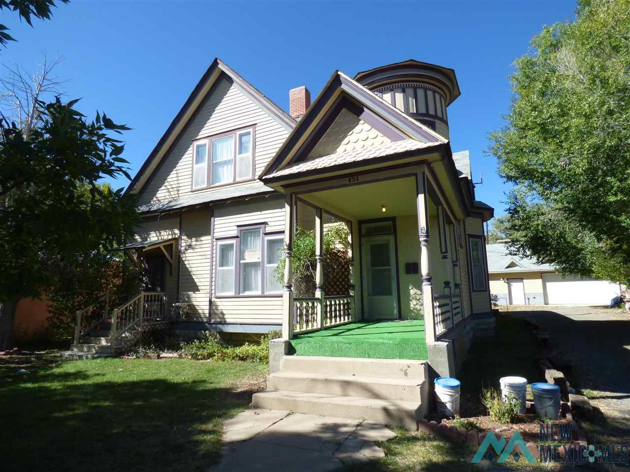 A large two-story house with a green porch, stairs, and a green lawn.