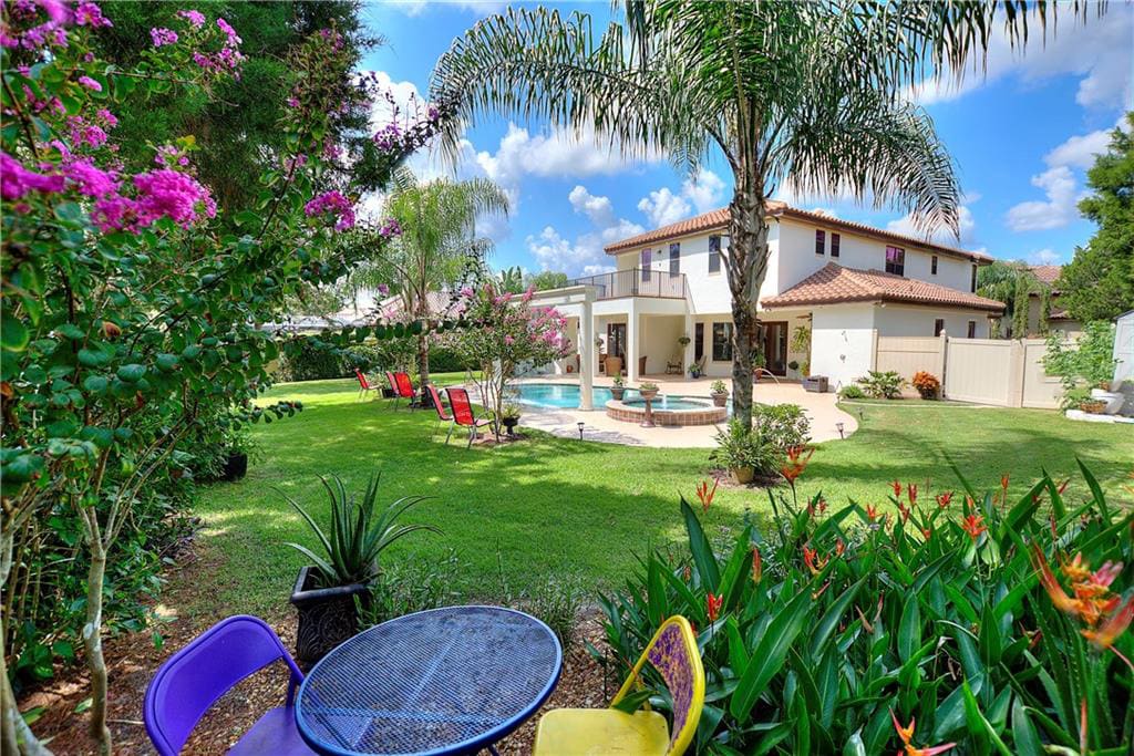 A backyard with a swimming pool, a table and chairs, and a large house in the background.