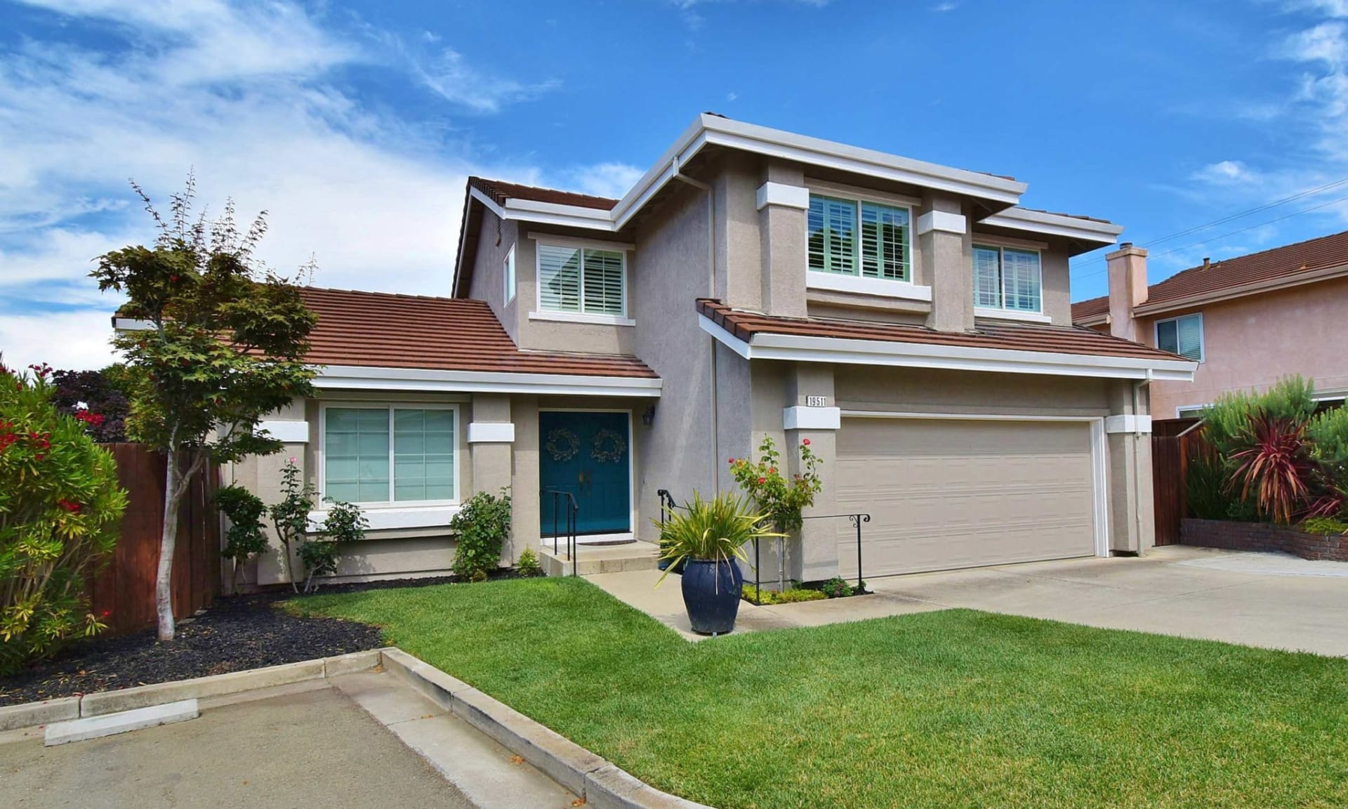 Two-story gray stucco home with a blue front door, tile roof, and two-car garage.