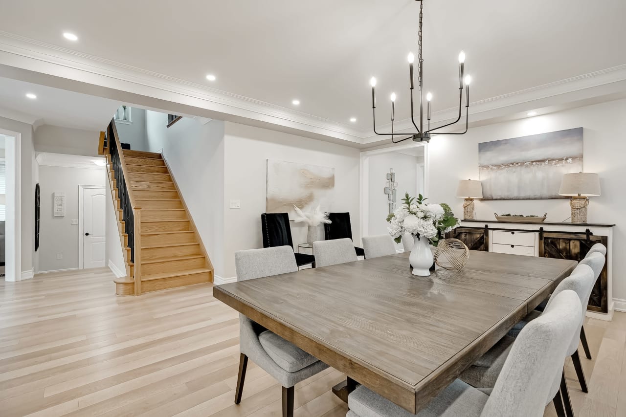 A dining room with a wooden table and eight chairs with the staircase in the background.