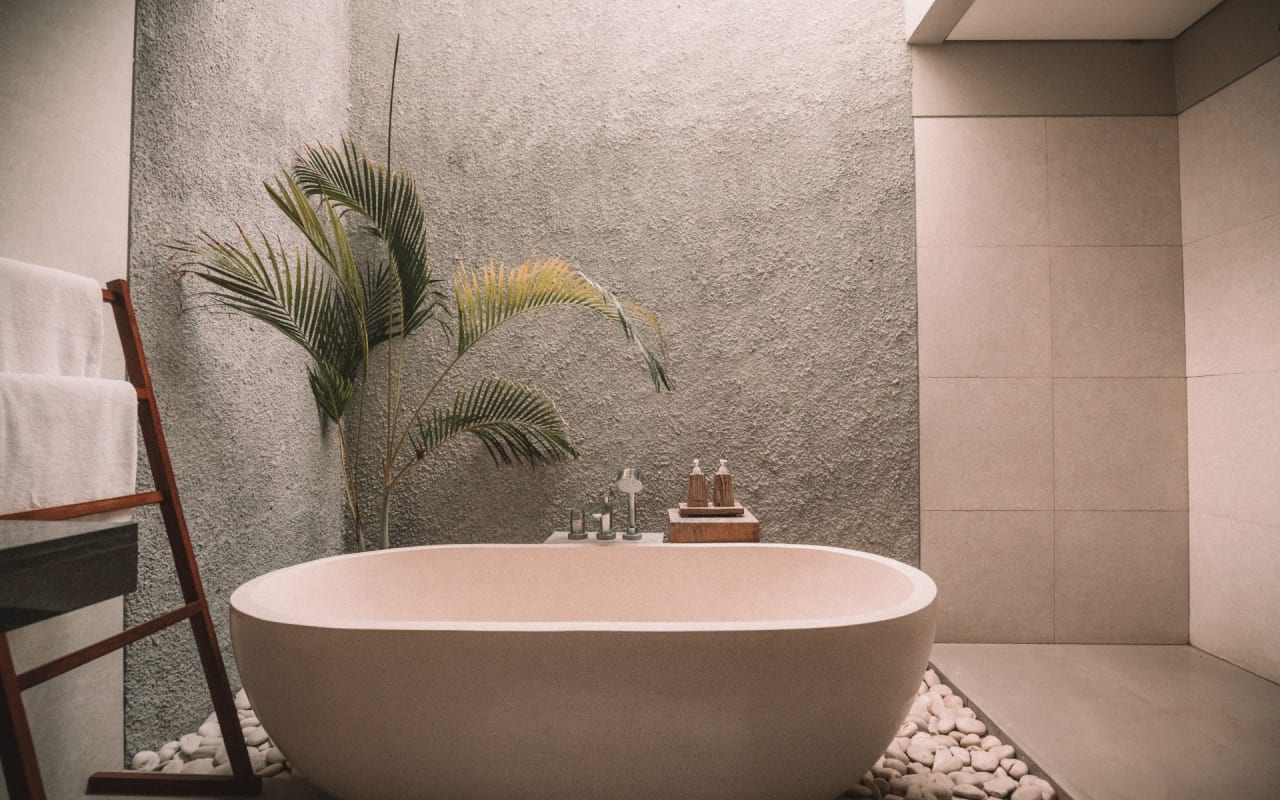 A bathroom with a large white bathtub next to a small palm tree.