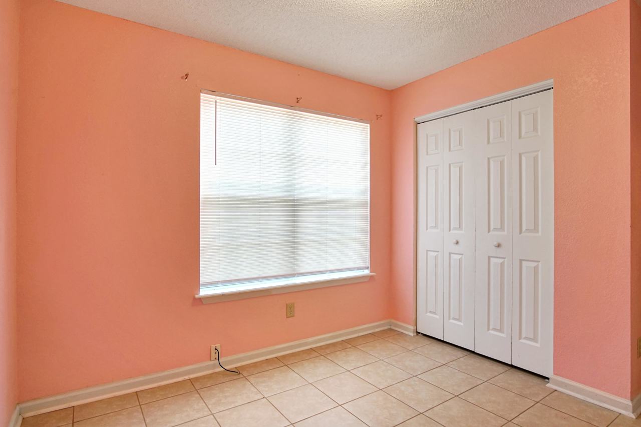 photo of third bedroom featuring peach walls, white ceiling, large window with white grid and blinds, a white double door closet, lightly colored tiled floors, and white baseboards at 2709 Oak Park Court, Tallahassee, Florida 32308