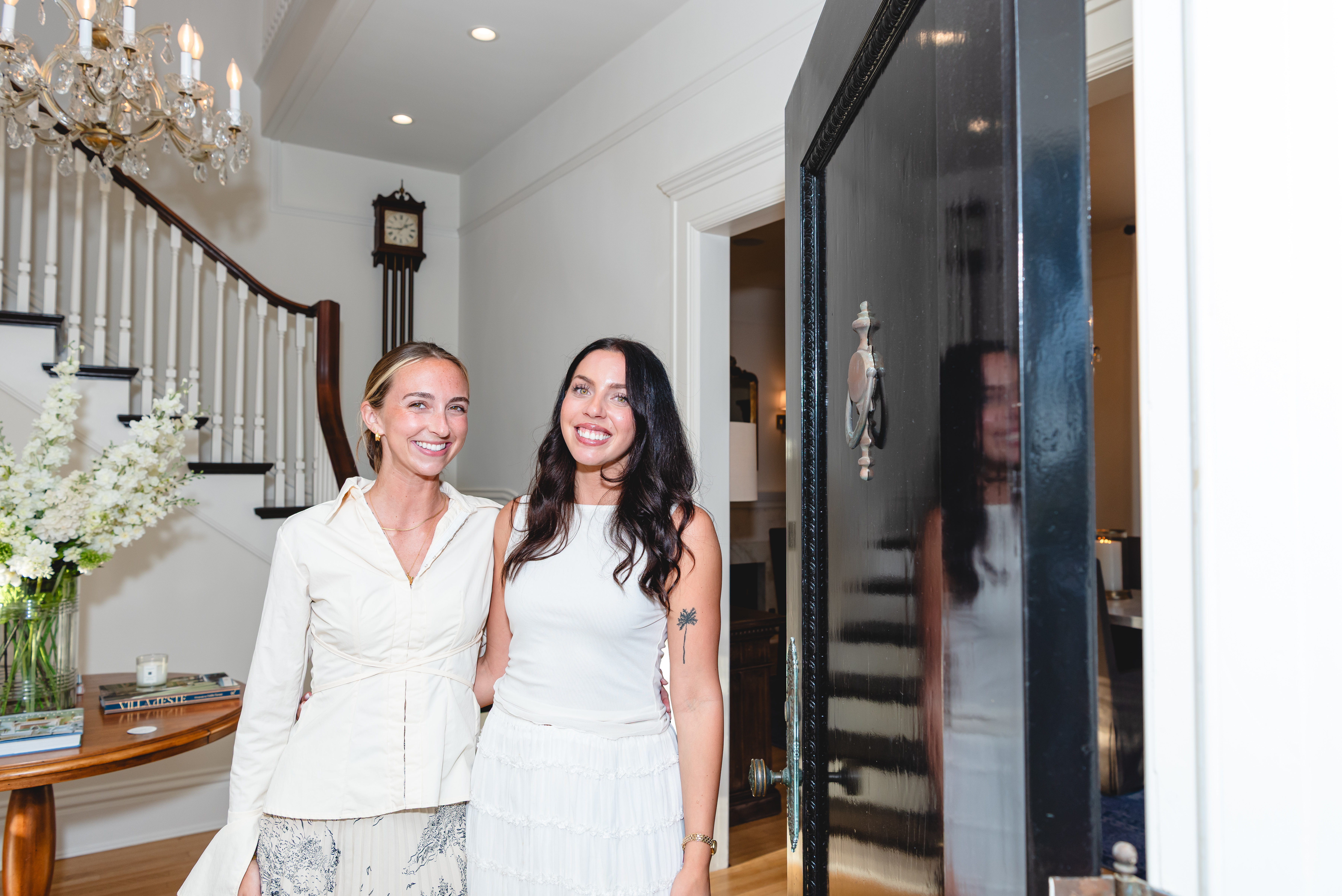 Two guests in the foyer beside the curved staircase and chandelier
