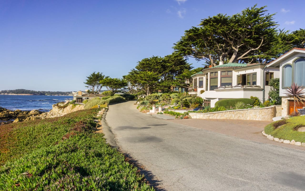 Oceanfront homes with white exteriors, wooden decks, and beach pathways surrounded by rocks and vegetation.