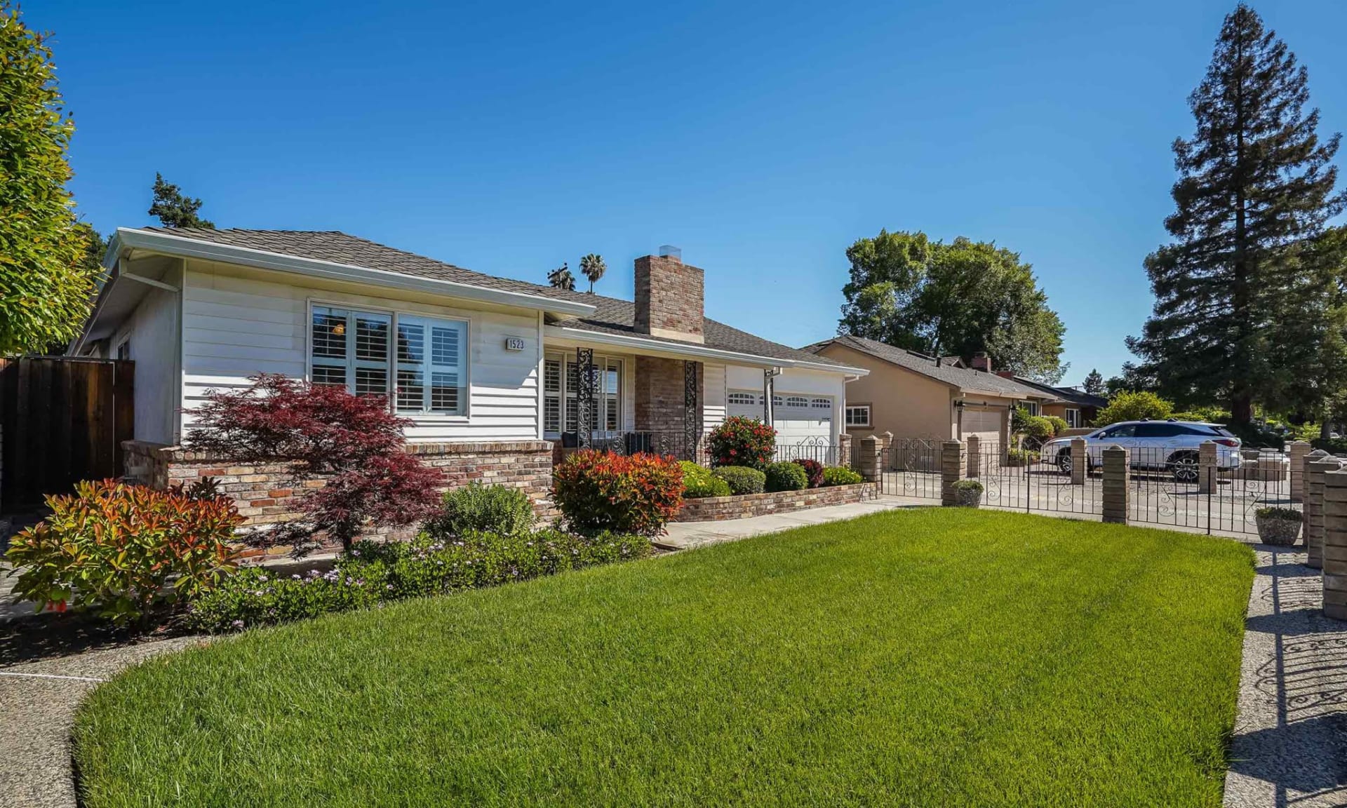 Single-story white house with a brick chimney, landscaped garden, and broad green lawn.