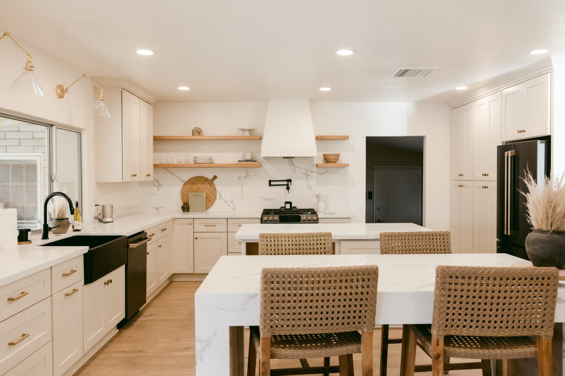Bright cream kitchen with a marble island, woven stools, and black appliances.