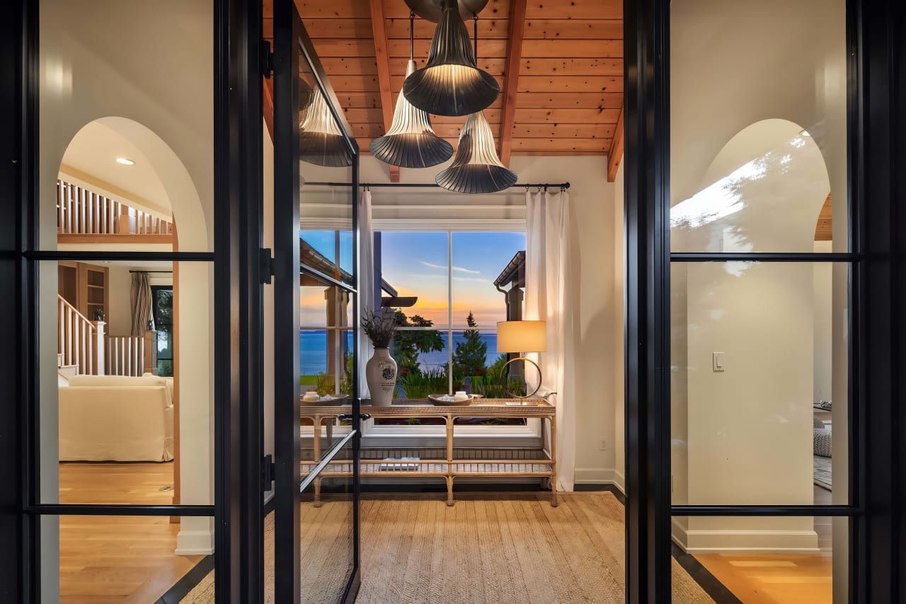 Elegant hallway with black-framed glass doors, a wooden console table, and a large window.