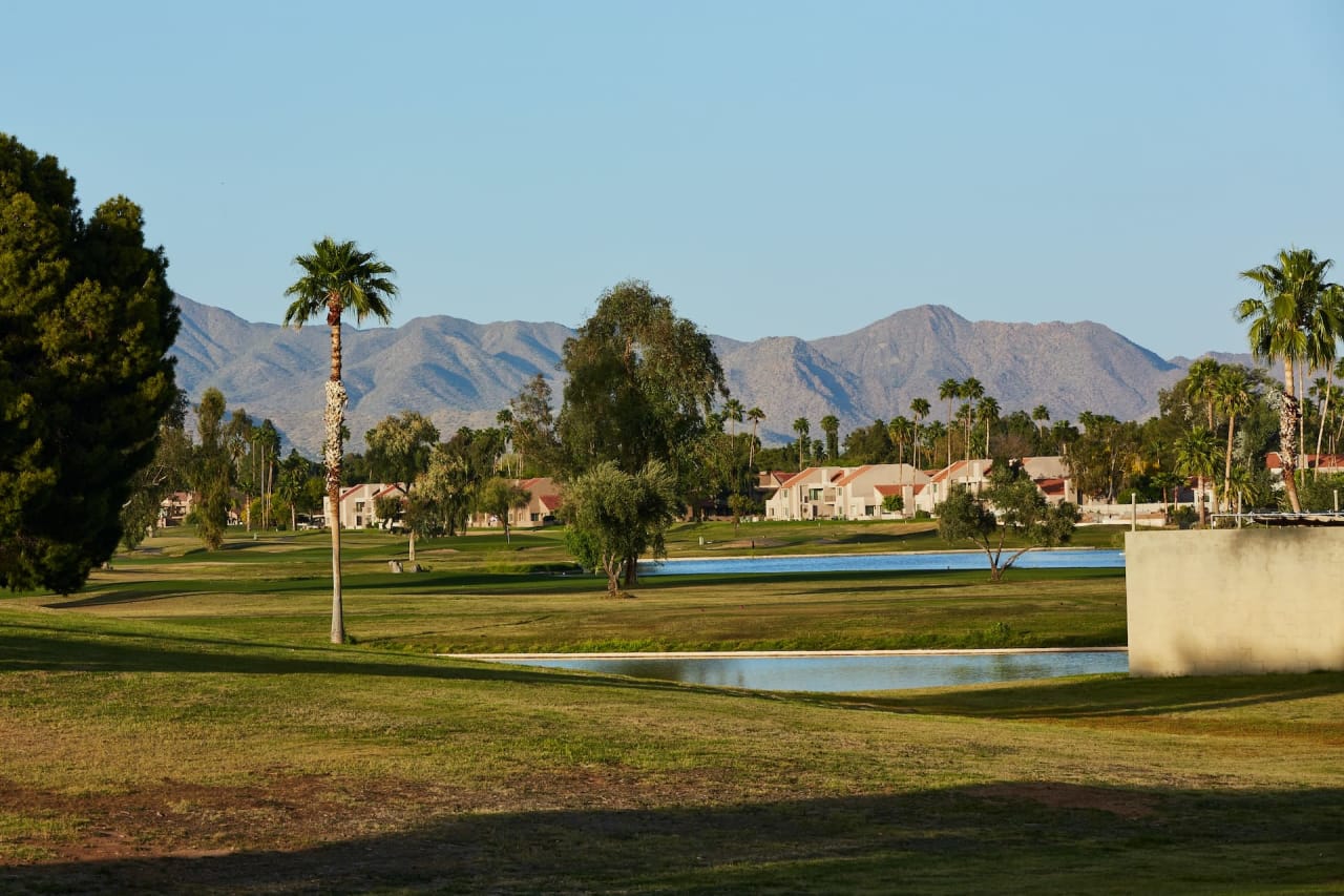 Golf course with palm trees, small lakes, and mountains in the background, surrounded by residential homes.