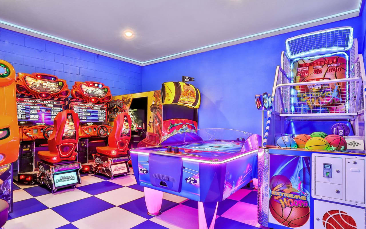 A game room filled with classic arcade games and a basketball hoop.