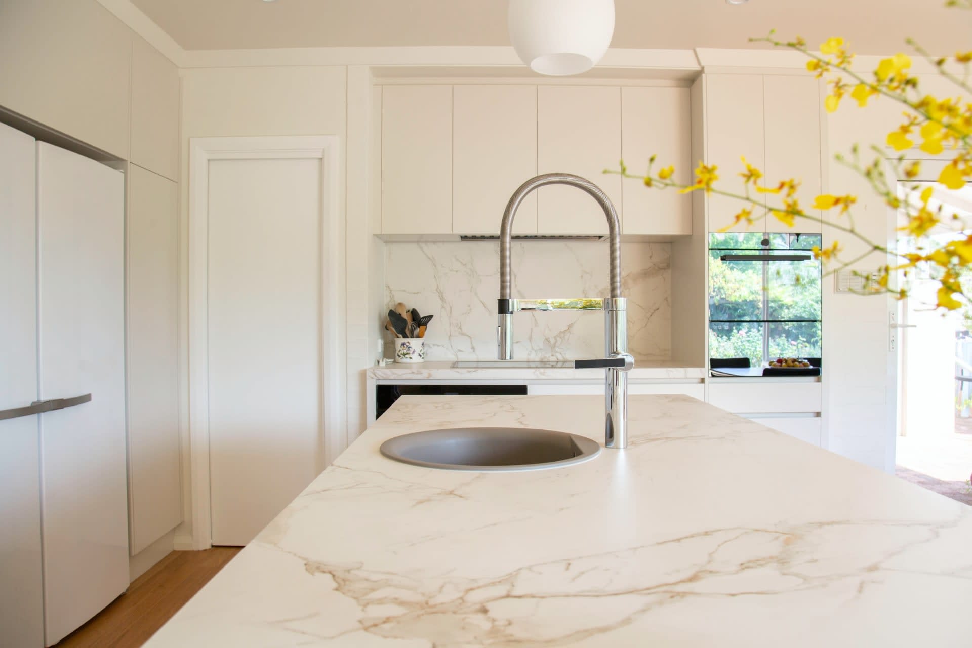  A modern kitchen featuring a large island with a white marble-patterned countertop and an integrated sink with a tall, curved silver faucet. 