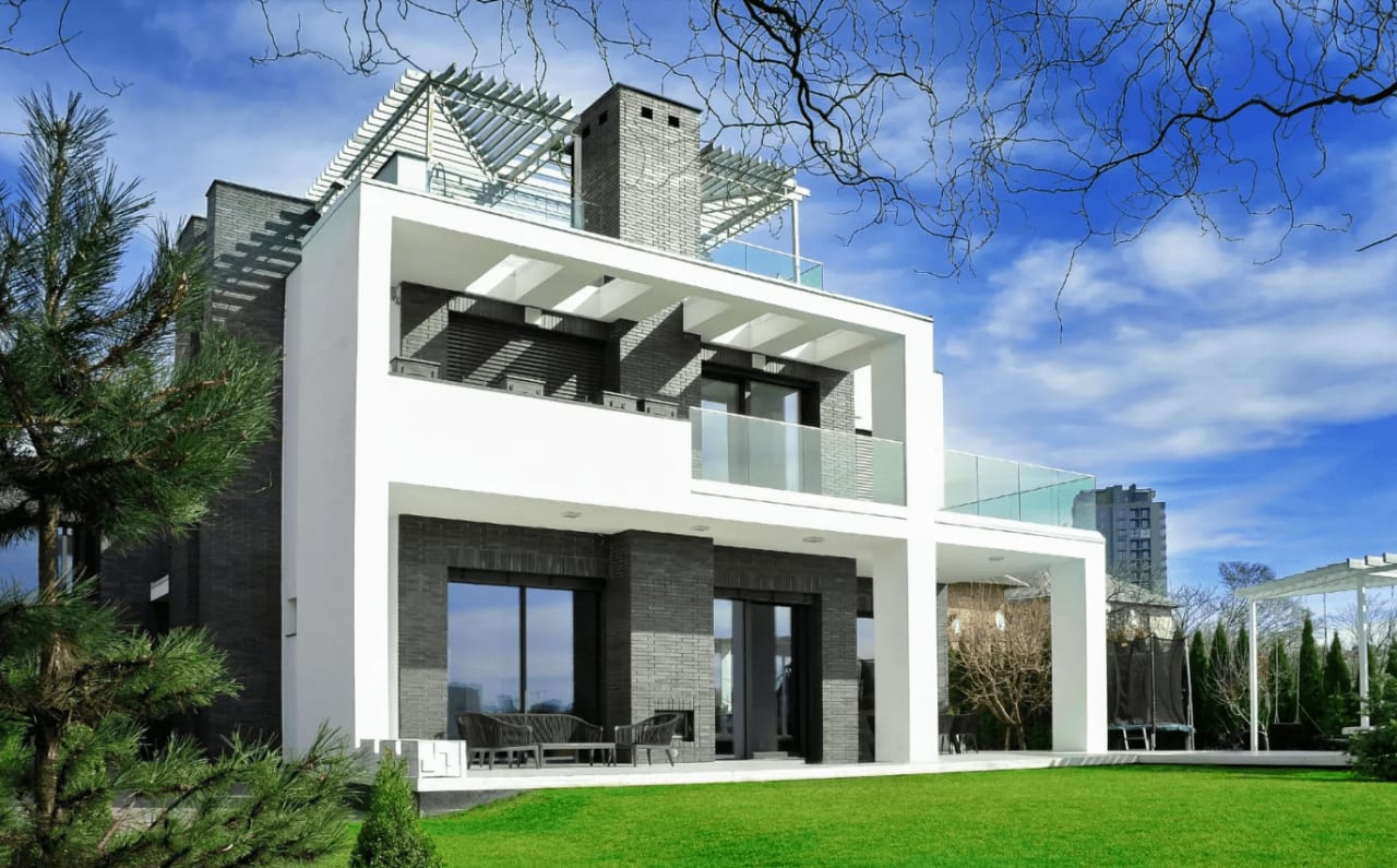 A modern house with a  2-car garage, spacious driveway, light facade, dark trim, red door, and lush greenery