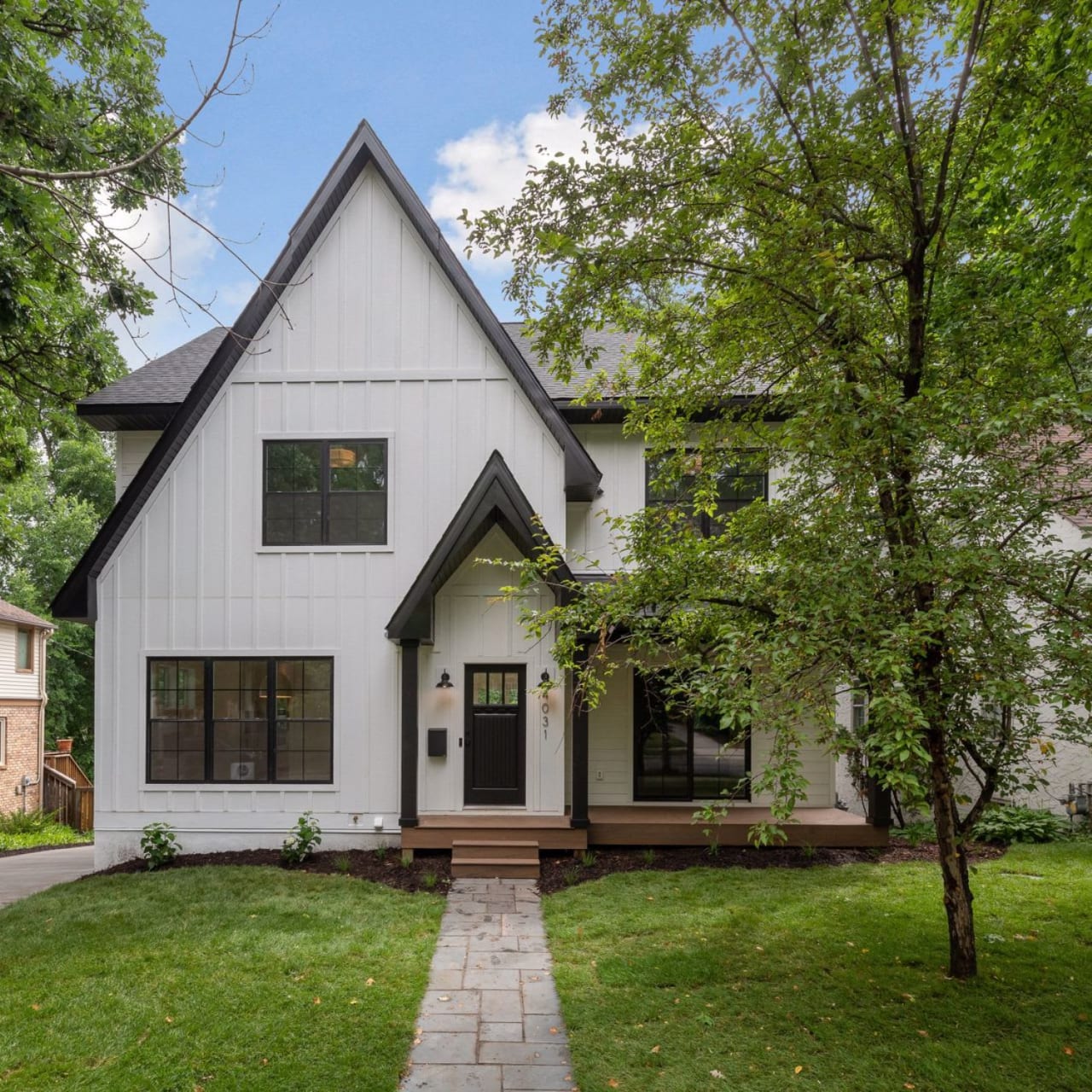 A white house with black windows and a tree in the front yard.