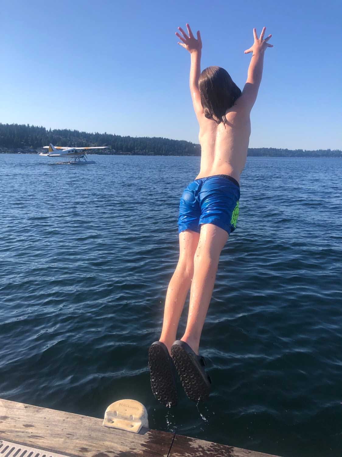 a kid in a blue swim shorts jumping towards the lake