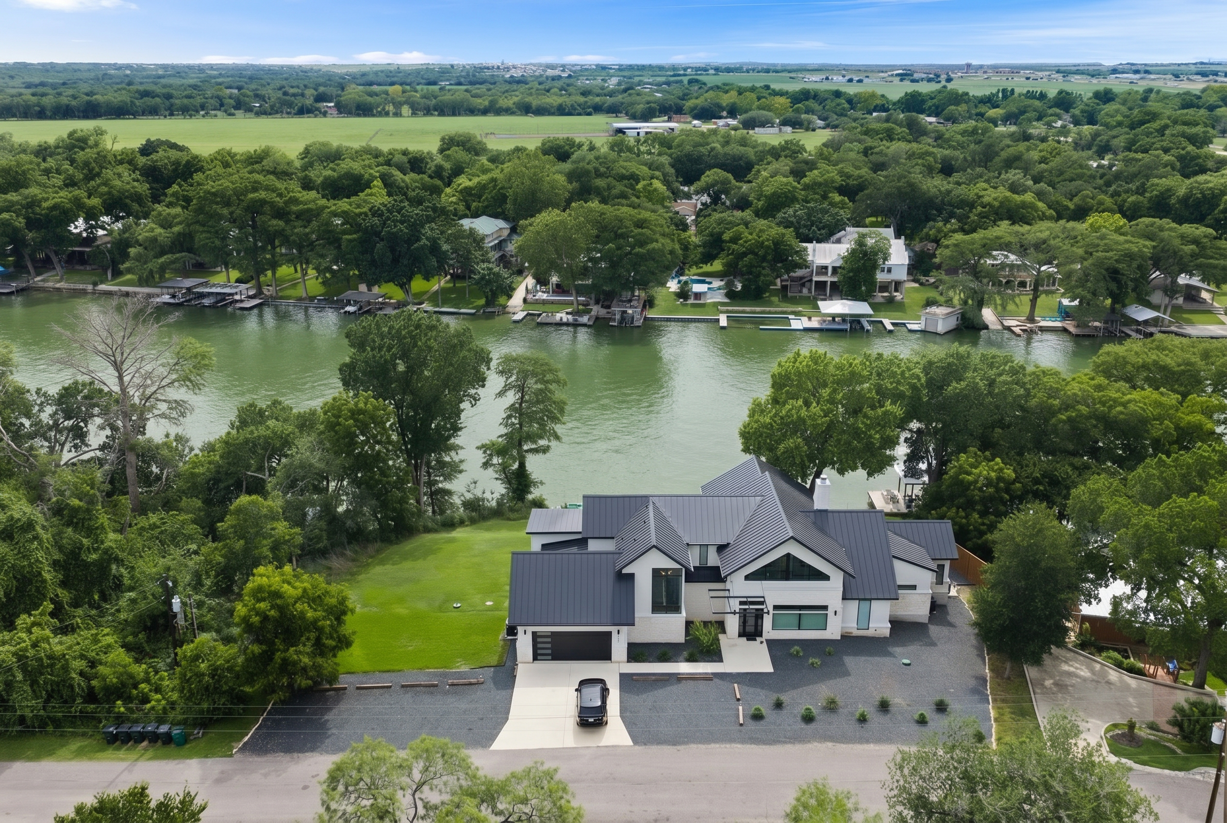 Daytime aerial view of a two-story white home with a dark metal roof on a green lot along Lake Placid, with docks and boathouses on the far shore