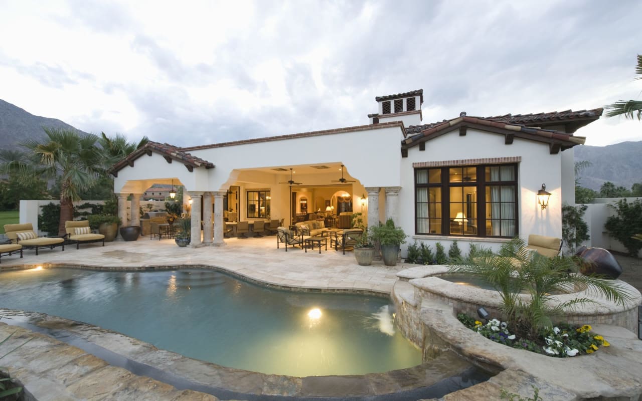 Luxury Spanish-style home with a swimming pool, covered outdoor seating area, and mountain views.