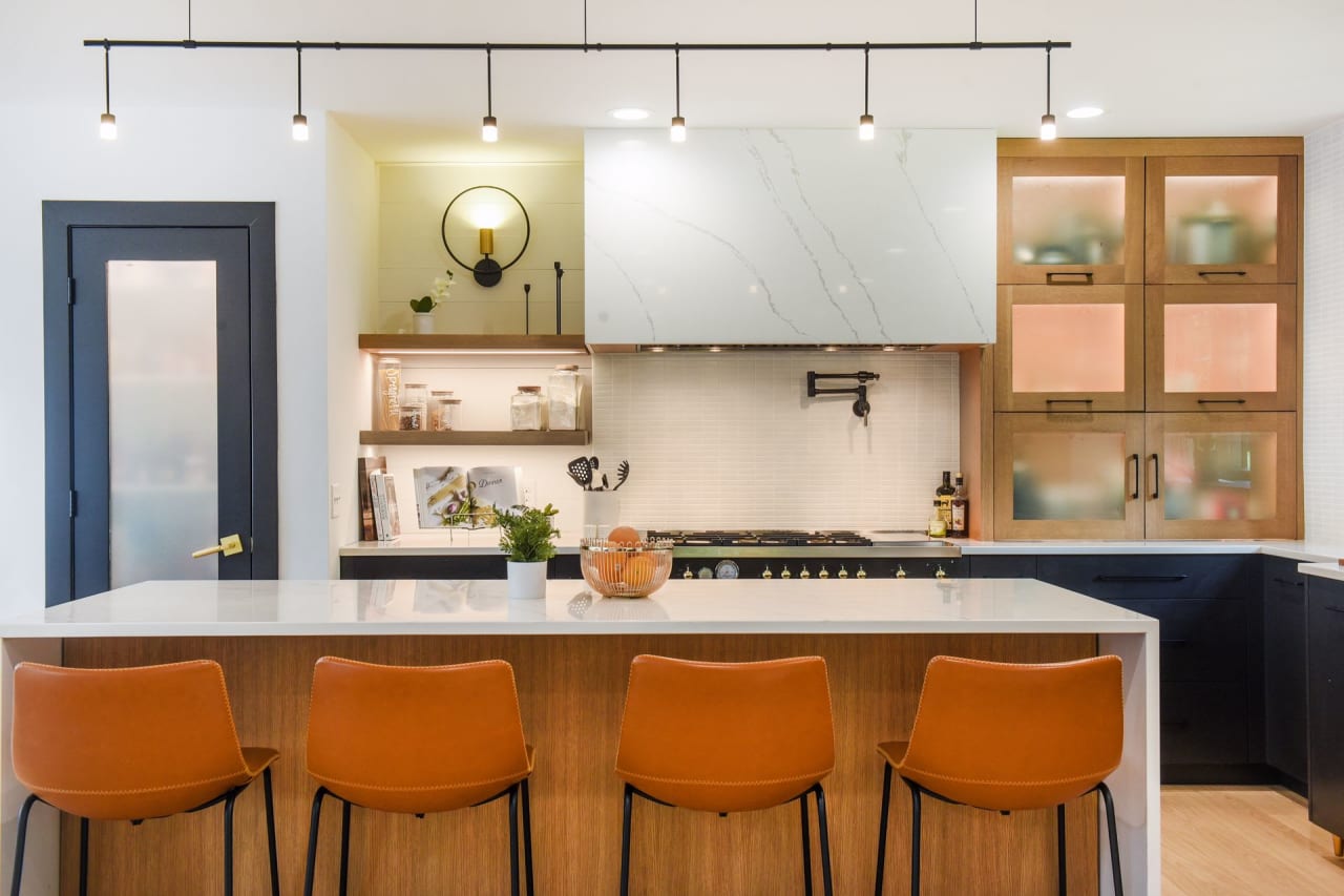 A well-lit kitchen with a large center island that has four stools pulled up to it.