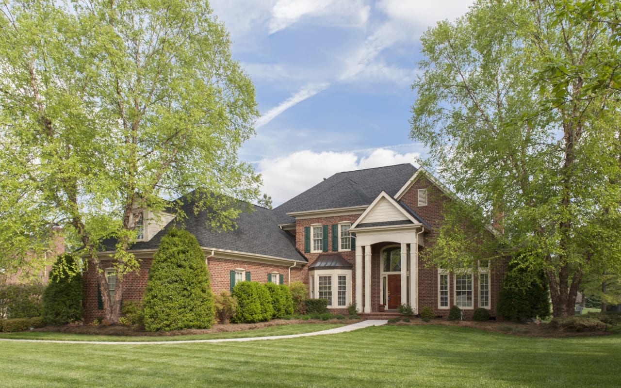 A large red brick house with white accents around the windows and doors, a green yard, and a paved walkway to the front door.