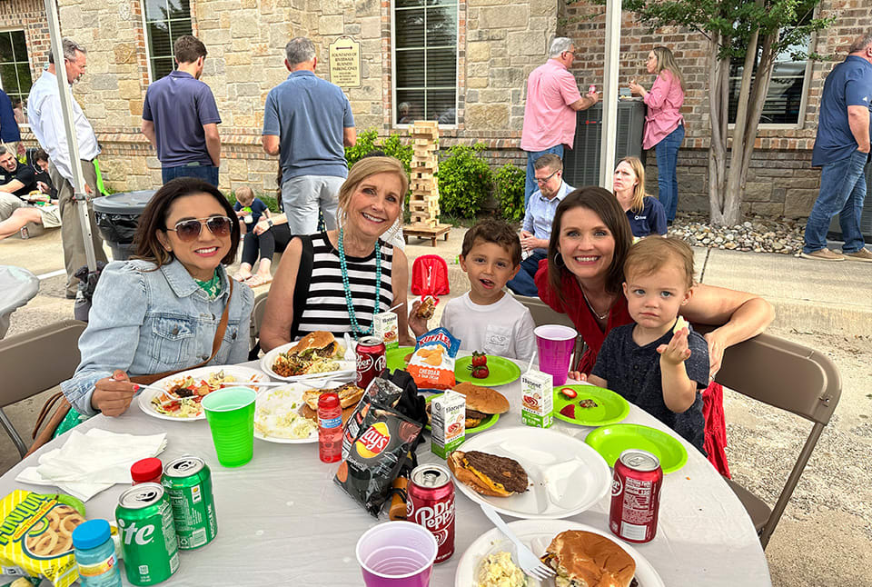 Women and children eating chips and burgers with a brick wall building in the background 