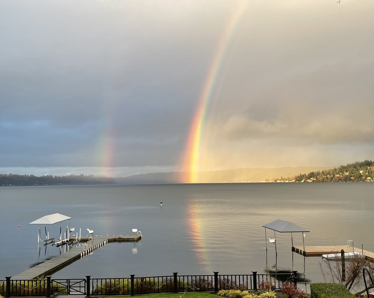 A rainbow over a lake with a dock and a fence