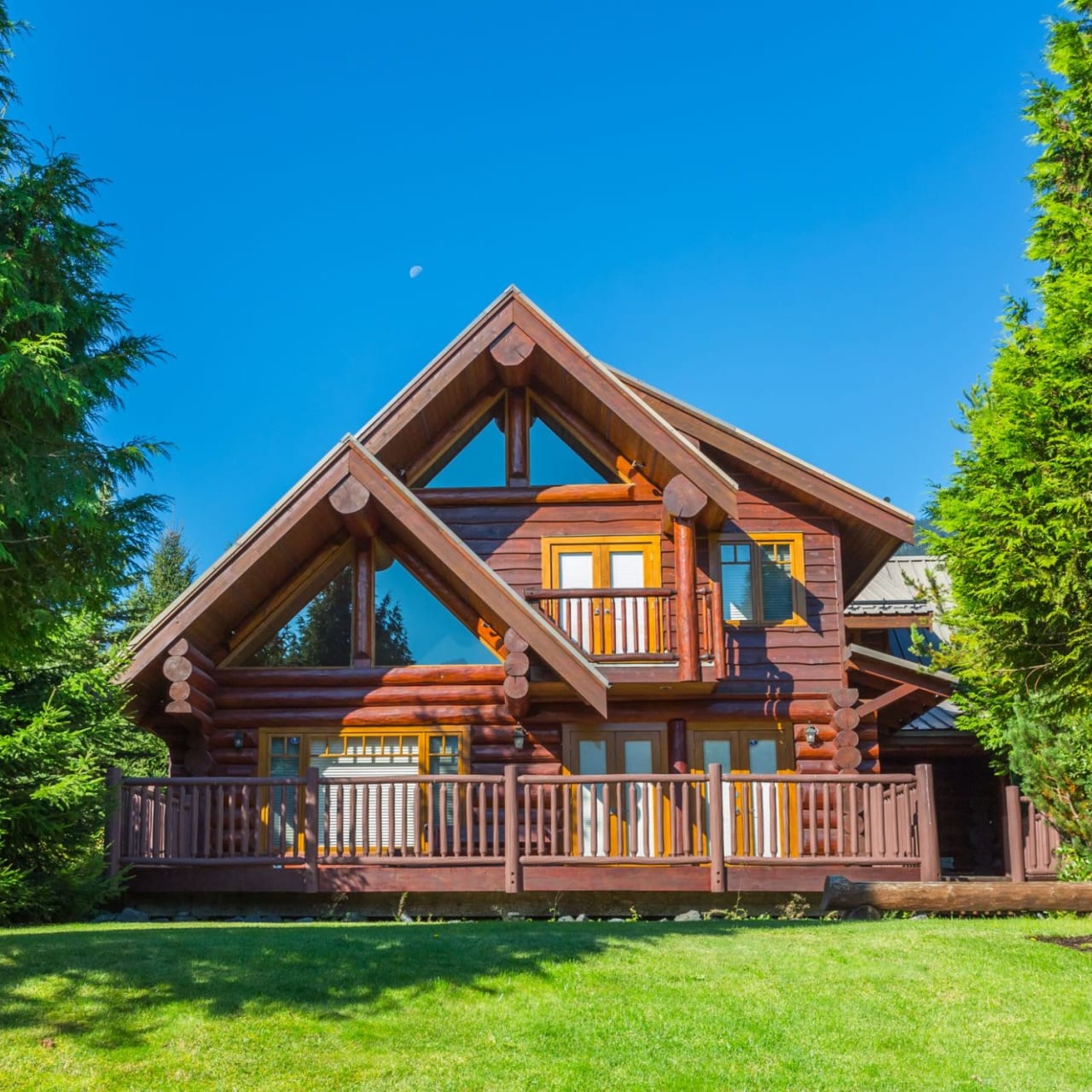 A large log home with a wraparound deck in a wooded area.