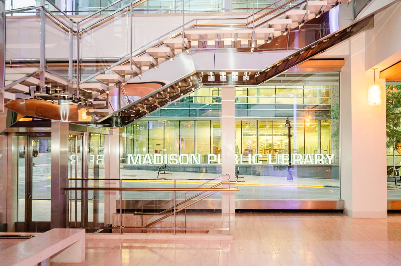 A brightly lit interior of a lobby with a staircase and an elevator.