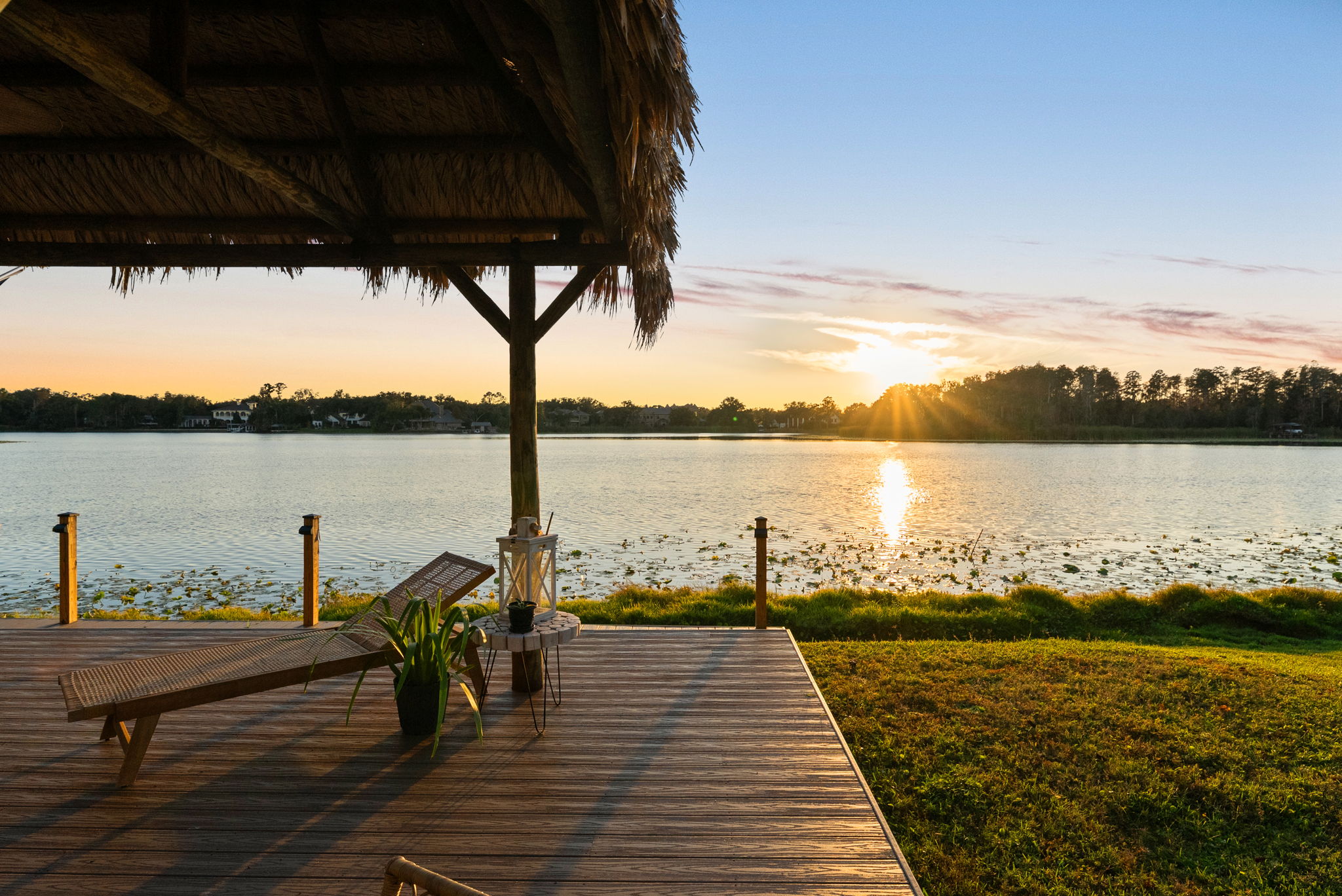 Waterfront dock with a lounge chair and tiki shelter at sunset over a Florida lake.