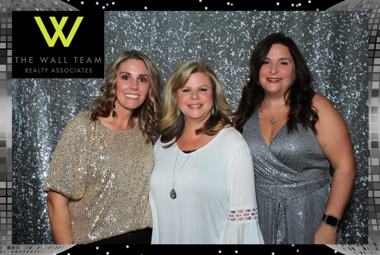 Three ladies in sparkling outfits posing in a photo booth with a black and white background