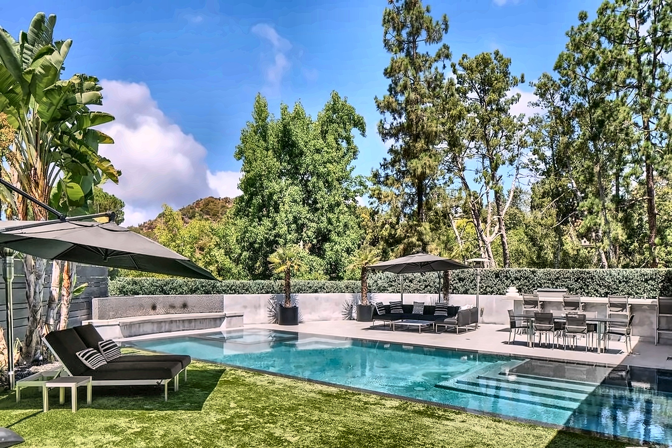 Private Beverly Hills backyard with a pool, lawn, hedges and canyon views framed by mature trees