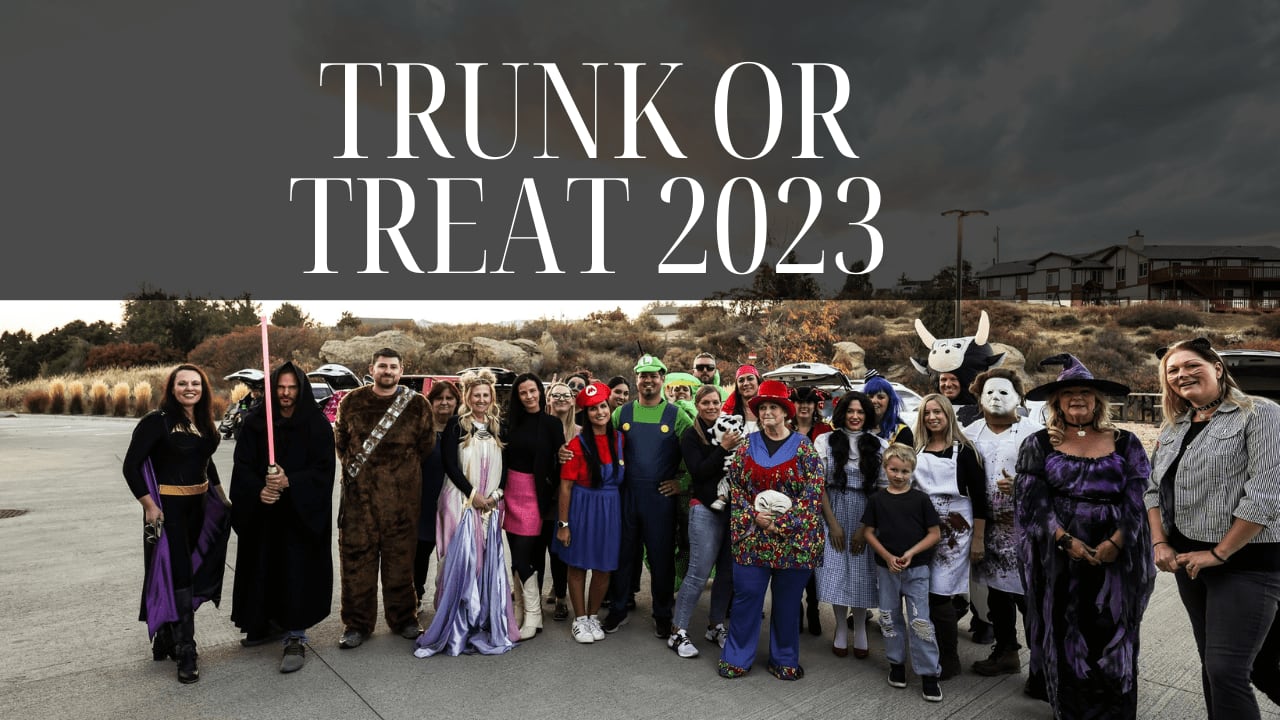 Group of people in Halloween costumes standing together under a cloudy sky at Trunk or Treat 2023 event.