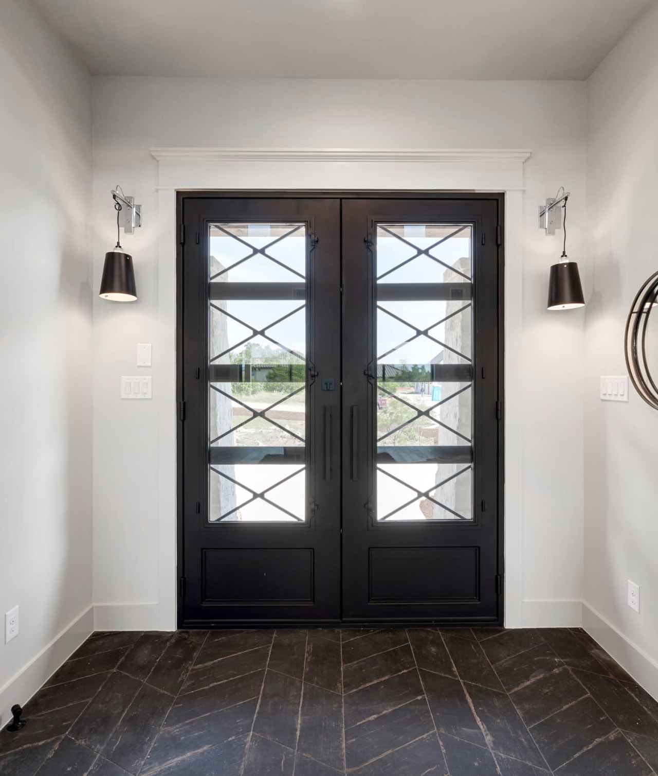 An entryway with a black wrought iron door and a patterned tile floor.