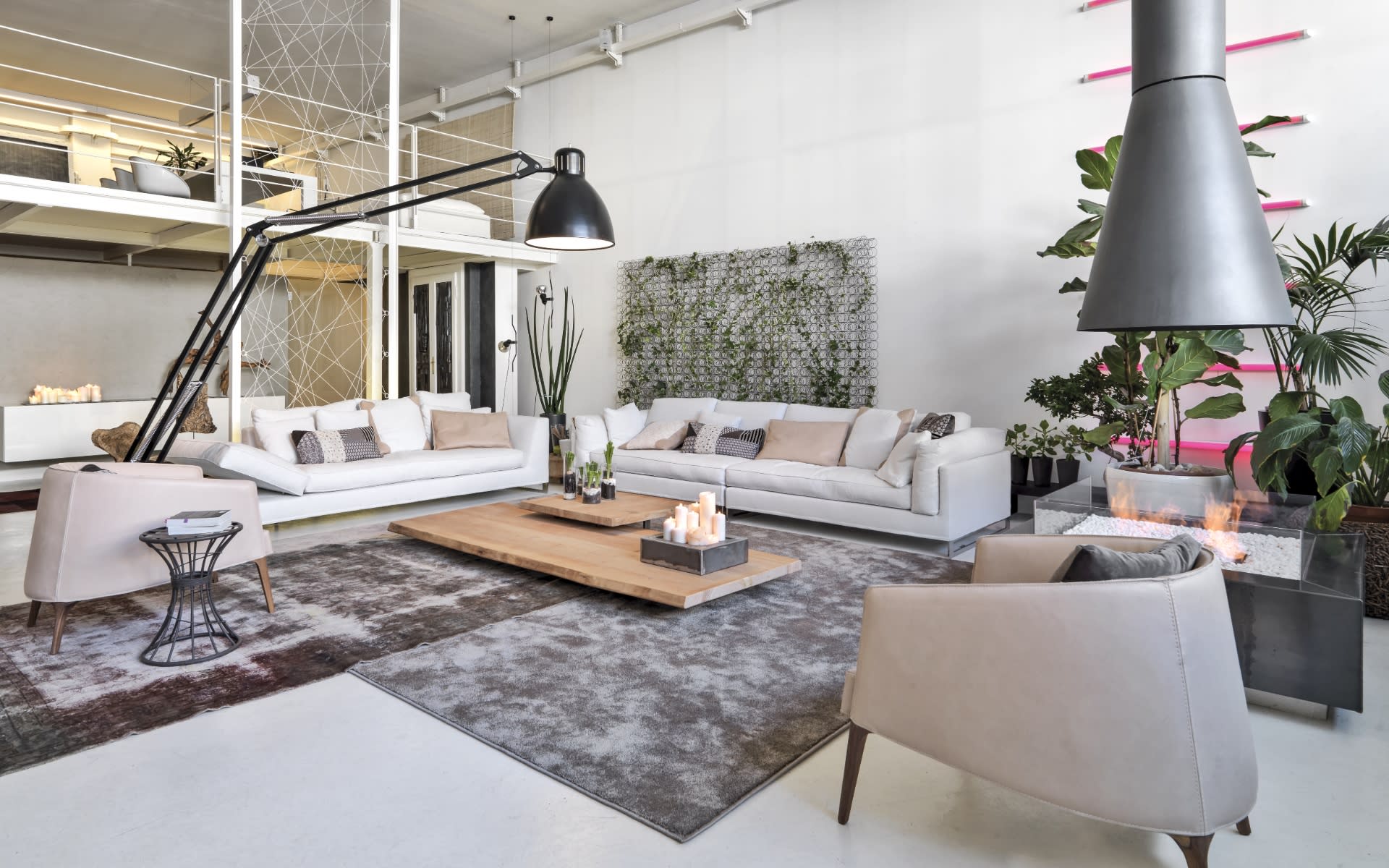  A spacious, modern loft living room features a striking industrial design with high ceilings and an open mezzanine level visible in the background. 