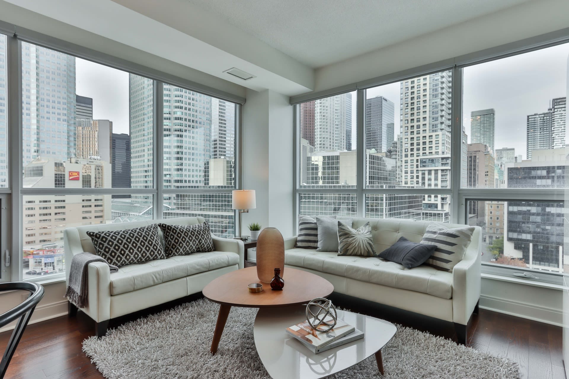 A modern living room with two light gray couches, a coffee table, and a view of the city.