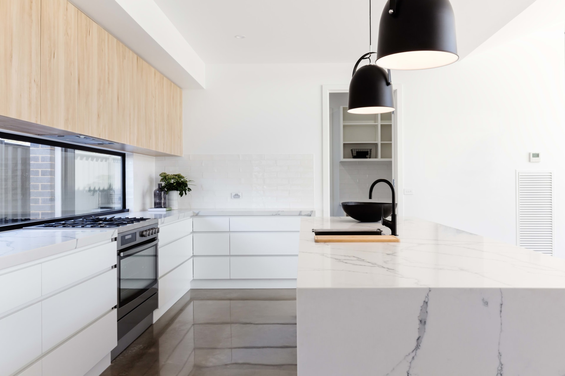 A kitchen with a stainless steel stove, single basin sink, white cabinets, pendant lights, and an outside-view window.