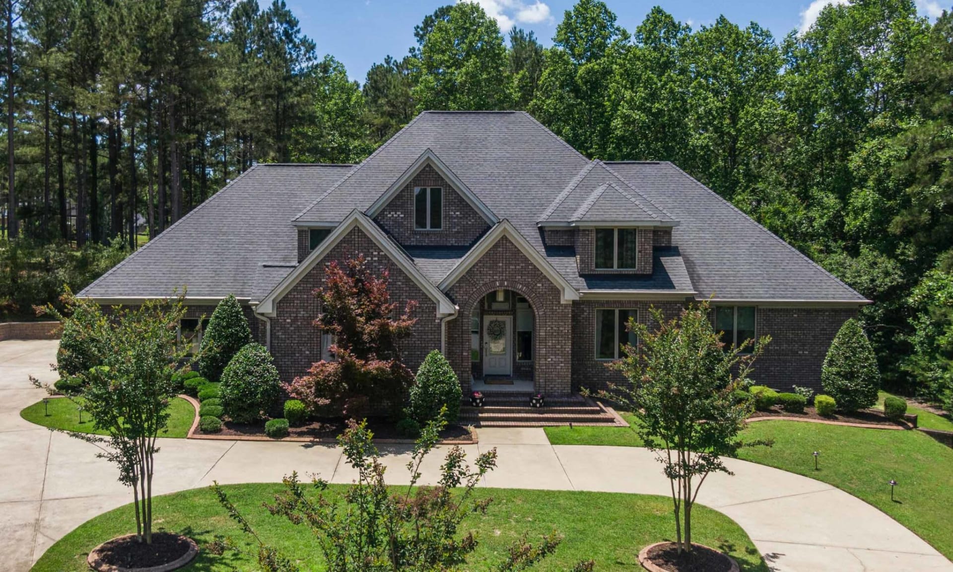 A large brick house with a driveway and trees in the background.