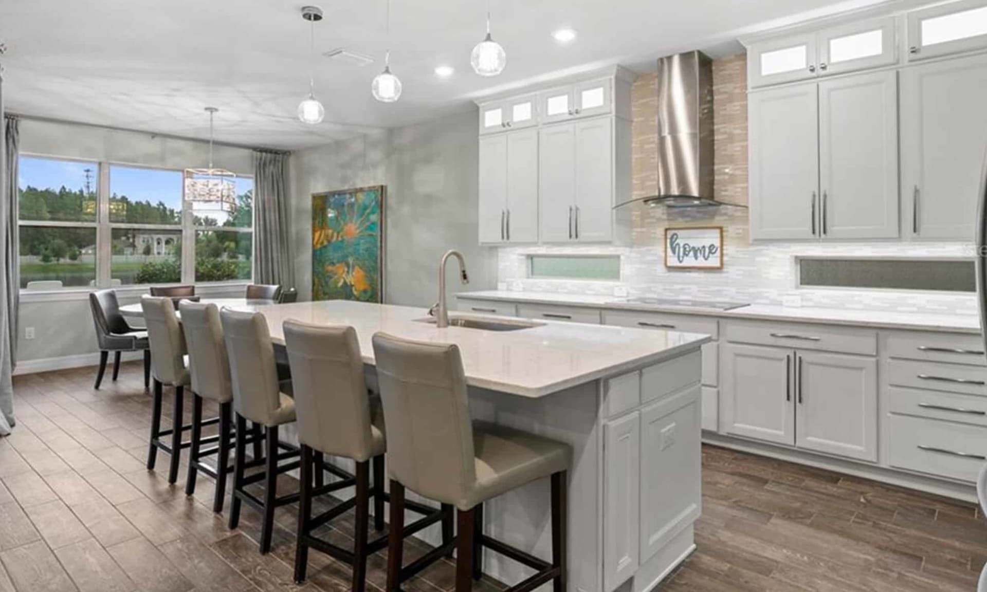 Modern white kitchen with a large island, bar seating, and windows overlooking trees.