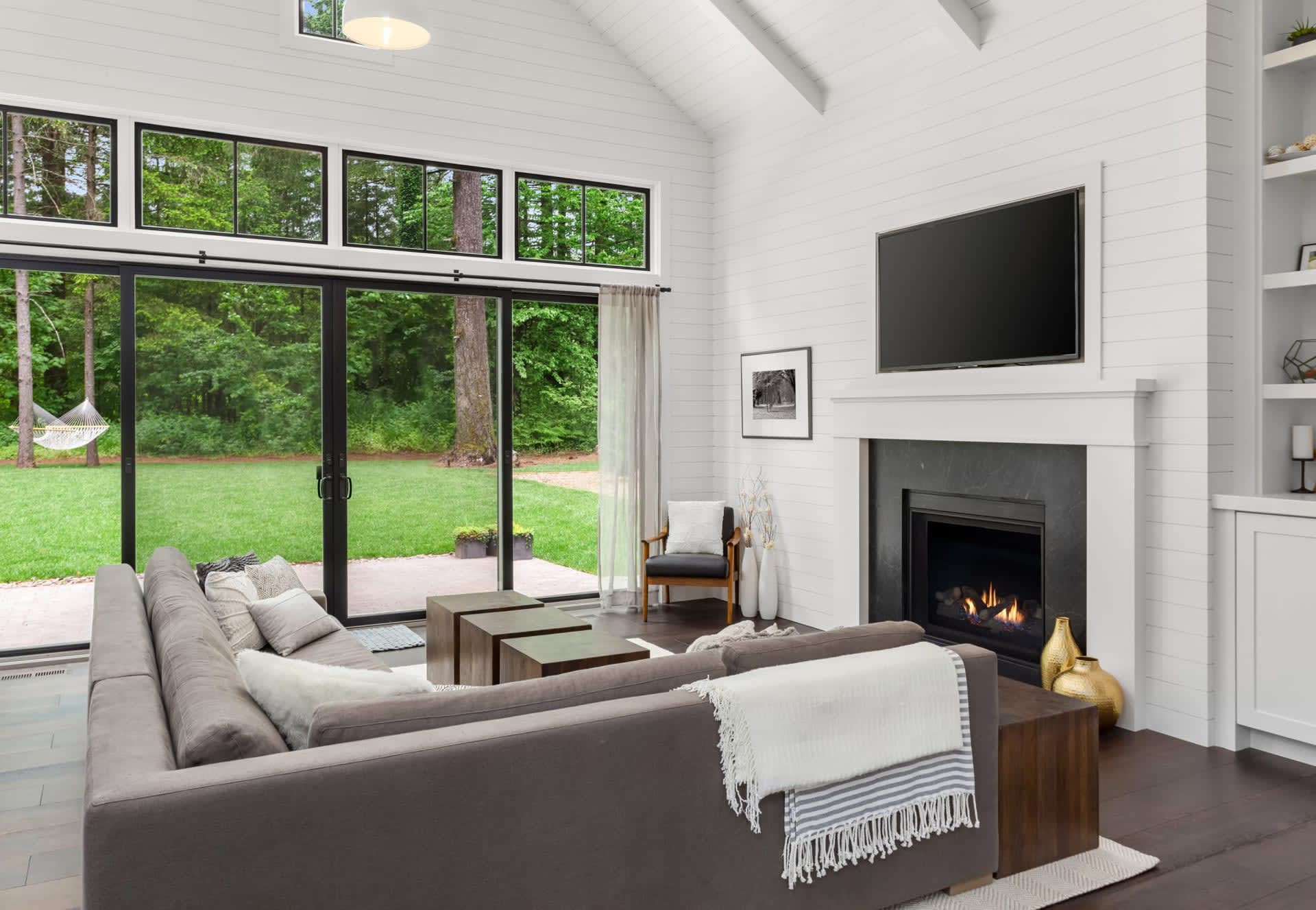 A living room with a large couch, coffee table, brick fireplace, wall-mounted television, and sliding glass doors to a patio.