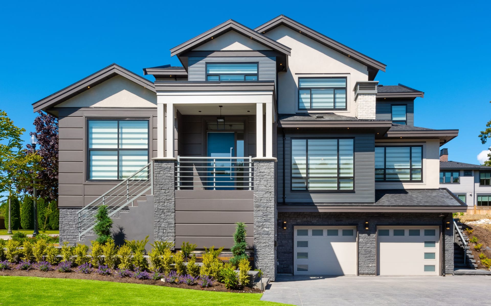 A large, two-story house with a gray roof, a black garage door, and a stone accent wall around the entrance and lower portion of the house