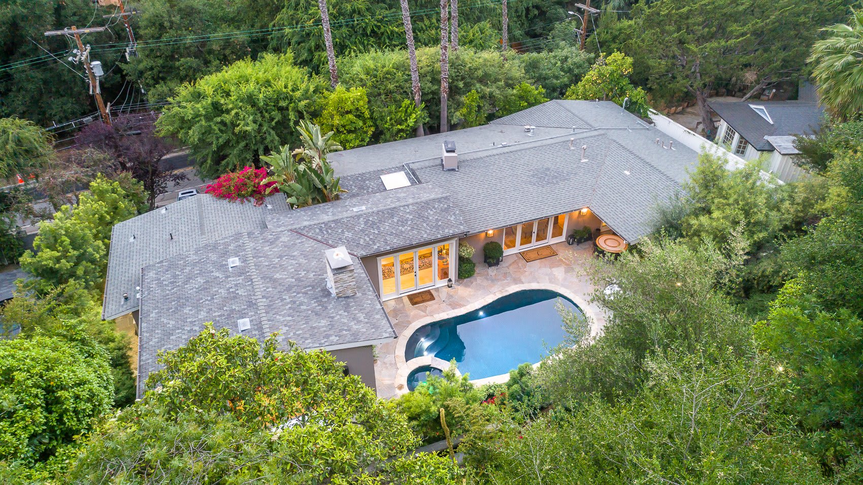 An aerial view of a two-story house with a swimming pool in the backyard. Trees surround the house, and it has a patio