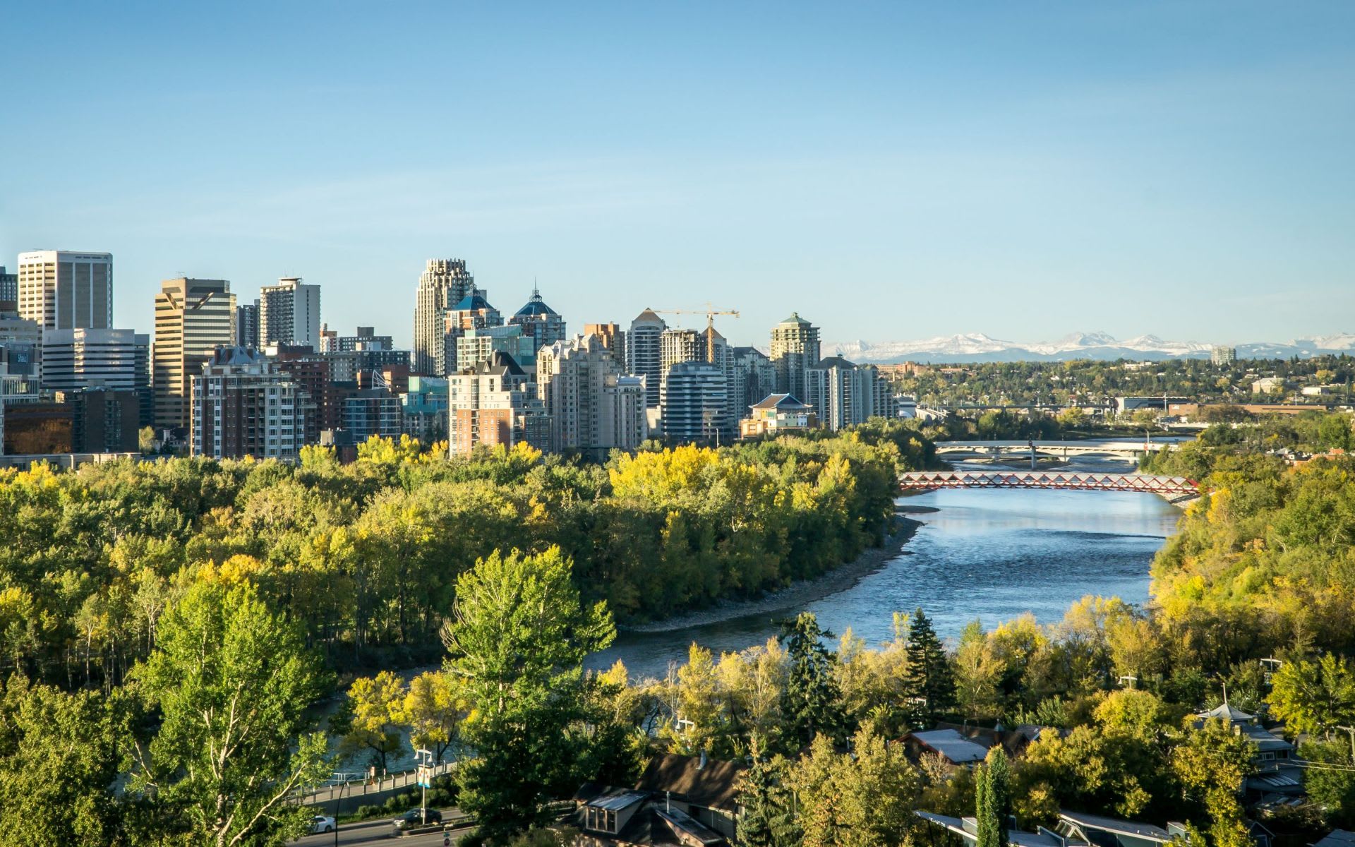 A city skyline with a river in the foreground and trees lining the riverbank