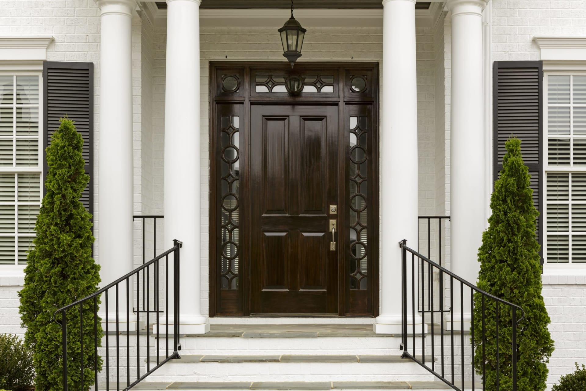 A front entryway of a house with white trim, stairs with black metal handles to the front door and rectangular windows.