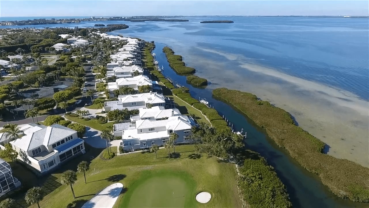 Aerial view of a vibrant golf course community with oceanfront homes and a marina