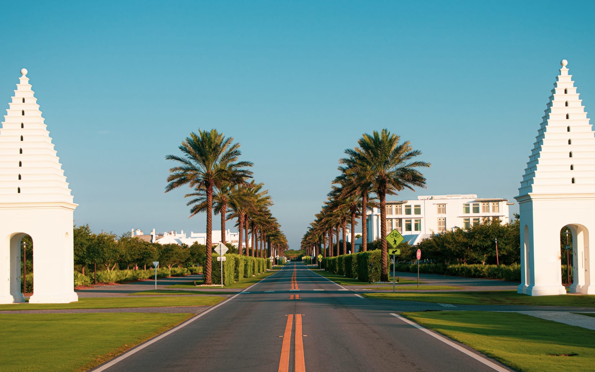 Palm-lined road framed by white entrance towers at Alys Beach